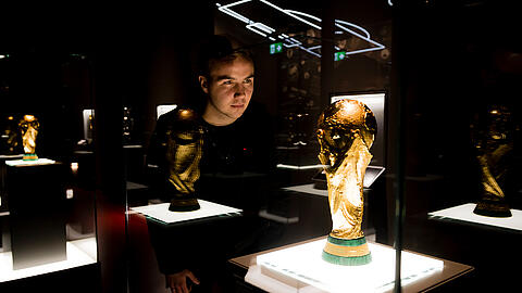 Mario Götze schaut durch die Vitrine in der Schatzkammer des Deutschen Fußballmuseums auf den WM-Pokal 2014