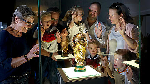Eine große Familie steht um die Vitrine mit dem WM-Pokal herum